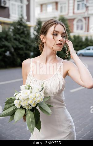 Junge Frau in Hochzeitskleid mit Blumenstrauß und wegblickend, Stockbild Stockfoto