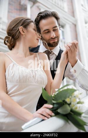 Porträt eines bärtigen Bräutigams, der Hand der Braut hält, mit Hochzeitsstrauß, Stockbild Stockfoto