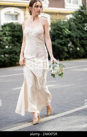 Lange junge Braut in weißem Kleid mit Hochzeitsstrauß mit Blumen, Stockbild Stockfoto