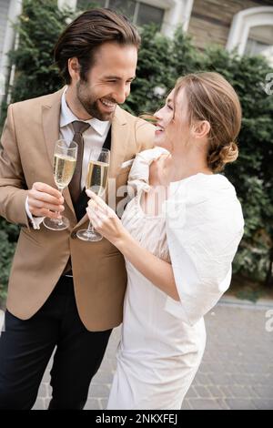 Fröhliche und junge Vermählte, die während der Hochzeitsfeier ein Glas Champagner klimperten, Stockbild Stockfoto