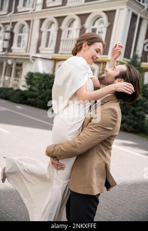 Bärtiger Bräutigam in formeller Kleidung, die fröhliche Braut in weißem Kleid draußen, Stock Image Stockfoto