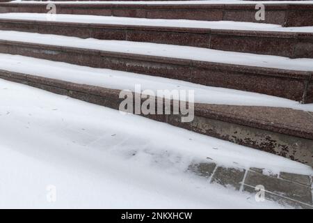 Granitbraune Treppen unter dem weißen Schnee. Stockfoto