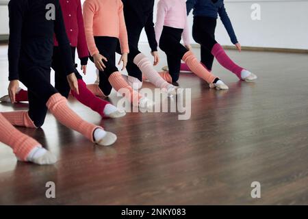 Zugeschnittene Bilder von Beinen von Kindern, die sich drinnen dehnen. Gymnastiktraining. Sportbegriff, Kindheit, rhythmische Gymnastik Stockfoto