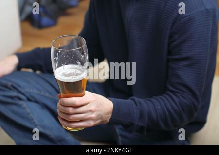 Eine Person hält eine Tasse mit Bier in der linken Hand vor sich Stockfoto