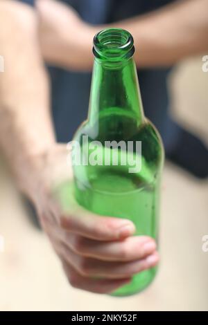 Eine Person hält eine grüne Flasche in der Hand vor dem Hintergrund von Holzbrettern Stockfoto