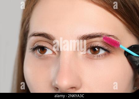 Kosmetikerin putzt die Augenbrauen von Frauen, bevor sie auf grauem Hintergrund abfärbt, Nahaufnahme Stockfoto