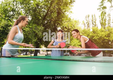 Glückliche Familie mit Kind, das Tischtennis im Park spielt Stockfoto