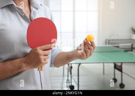 Geschäftsmann mit Tennisschläger und Ball neben Tischtennistisch im Büro, Nahaufnahme Stockfoto