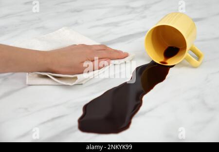 Eine Frau, die verschütteten Kaffee auf dem weißen Marmortisch reinigte Stockfoto