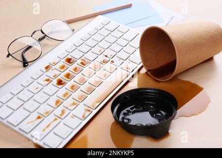 Eine Tasse Kaffee wurde über die Computertastatur auf dem hölzernen Büroschreibtisch verschüttet Stockfoto