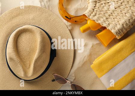 Strohhut, Sonnenbrille, Handtuch und Tasche mit Sonnencreme auf Sand, flach liegend Stockfoto