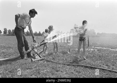 Arbeiter bewässerte ein Feld während der europäischen Hitzewelle von 1976, Kinder kühlen sich im Sprühwasser ca. 5. Juli 1976 Stockfoto