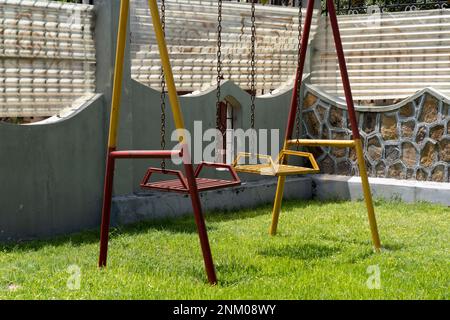 Alte und rostige Kinderschaukel. Rot und gelb lackiert. Kinderspielplatz. Stockfoto