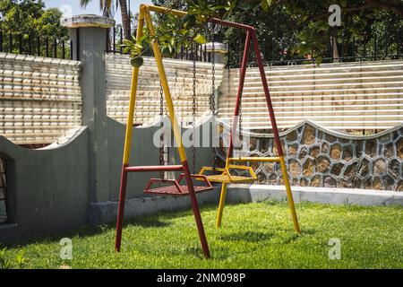 Alte und rostige Kinderschaukel. Rot und gelb lackiert. Kinderspielplatz. Stockfoto