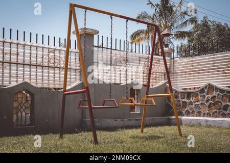 Alte und rostige Kinderschaukel. Rot und gelb lackiert. Kinderspielplatz. Stockfoto