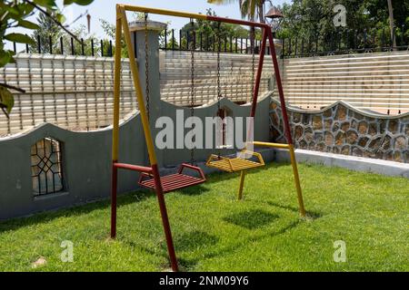 Alte und rostige Kinderschaukel. Rot und gelb lackiert. Kinderspielplatz. Stockfoto