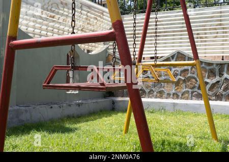 Alte und rostige Kinderschaukel. Rot und gelb lackiert. Kinderspielplatz. Stockfoto