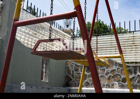 Alte und rostige Kinderschaukel. Rot und gelb lackiert. Kinderspielplatz. Stockfoto