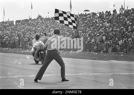 TT in Assen, Motorradrennen der 500cc. Klasse, Mann winkt mit der karierten Flagge. Wil Hartog überquert die Ziellinie auf dem dritten Platz ca. 26. Juni 1976 Stockfoto