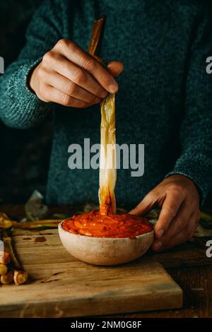 Nahaufnahme eines Mannes, der eine geröstete kalkotte, eine süße Zwiebel, typisch für Katalonien, Spanien, in Romesco-Sauce taucht, wie es üblich ist Stockfoto