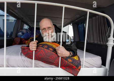 Dresden, Deutschland. 24. Februar 2023. Ein Mann liegt auf einem Bett, das während der Pressekonferenz vor Beginn der 33. stattfindenden Rallye Dresden-Dakar-Banjul in der Werft Laubegast in sein Fahrzeug eingebaut wurde. Die Rallye Dresden-Dakar-Banjul beginnt am 25. Februar 2023 in Hohnstein (Sachsen) mit dem Ziel Gambia, wo die Fahrzeuge versteigert und die Erlöse an die NRO „Dresden-Banjul Organization“ gespendet werden. Kredit: Daniel Schäfer/dpa/Alamy Live News Stockfoto