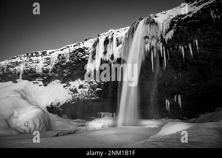 Eine faszinierende Winterszene mit einem malerischen Wasserfall, der einen felsigen Berghang hinunterragt, mit Eiszapfen und eisigen Wasserströmen, die von den Seiten fließen Stockfoto
