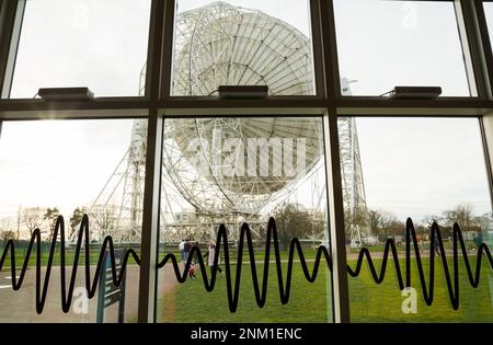Das riesige Lovell-Radioteleskop am Jodrell Bank-Standort in Cheshire, Großbritannien. Vom Fenster des Besucherzentrums aus gesehen, das mit Radiowellen-Grafiken dargestellt wird. Der Rahmen, der die Schale stützt, ist von hinten/rückwärts/seitlich deutlich zu sehen. (133) Stockfoto