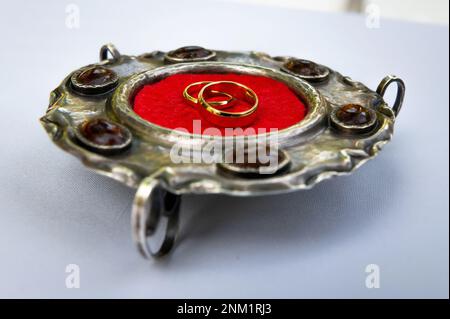 Eheringe und Details Eheringe auf einer silbernen antiken Platte mit Bernstein- und rotem Wildlederzentrum Stockfoto