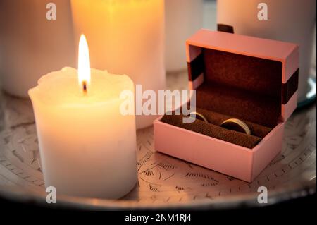 Eheringe und Details eine pinkfarbene Schachtel für Eheringe liegt auf einer Silberplatte zwischen beleuchteten Kerzen Stockfoto
