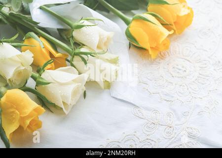 Frohe Ostern. Ostereier auf einem rustikalen Tisch mit weißen und gelben Rosen. Natürlich gefärbte, farbenfrohe Eier auf Holzteller und Frühlingsblumen in rustikalem Raum. Stockfoto