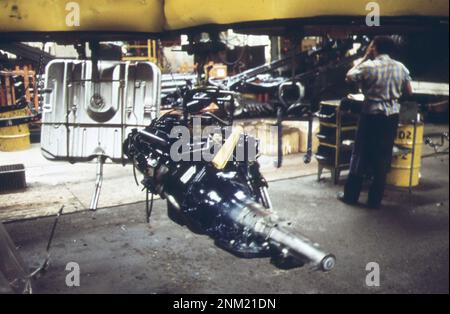 1970er Amerika: An der Cadillac-Montagelinie – Motoren und Kraftstofftanks, die auf Drähten aufgehängt sind, treiben durch das Werk, auf dem Weg zur Montage an den Karosserien ca. 1973 Stockfoto