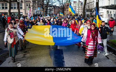 Hamburg, Deutschland. 24. Februar 2023. Teilnehmer einer Demonstration gegen den Krieg in der Ukraine bewegen sich mit einer großen Flagge durch das Stadtzentrum. Die russische Armee war am 24.02.2022 in die Ukraine eingedrungen. Kredit: Daniel Bockwoldt/dpa/Alamy Live News Stockfoto