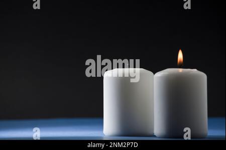 Zwei brennende Kerzen auf einem blauen Tisch mit schwarzem Hintergrund Stockfoto