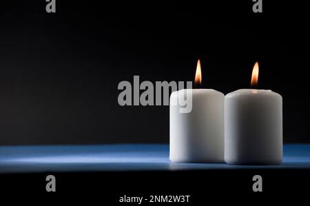 Zwei brennende Kerzen auf einem blauen Tisch mit schwarzem Hintergrund Stockfoto