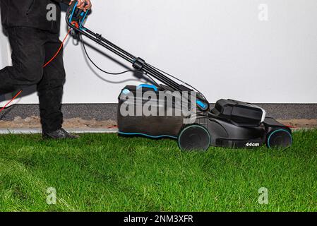 Ein Mann mäht das Gras mit einem Elektromäher mit einer Schnittbreite von 44 Zentimetern und einer Leistung von 1800 Watt. Stockfoto