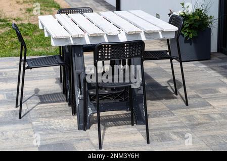 Terrassentisch aus weißer Palette auf Kunststoffböcken, schwarze Plastikstühle. Stockfoto