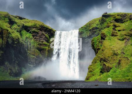 Majestätischer Skogafoss-Wasserfall mit Regenbogen und stimmungsvollem Himmel im Sommer in Island. Isländischer berühmter Ort, beliebte Attraktion der Landschaft Stockfoto