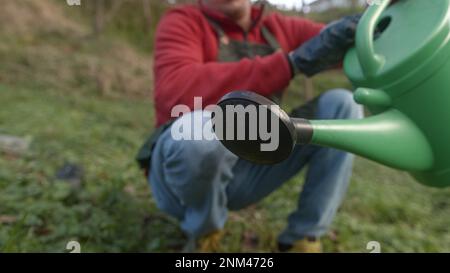 Junger männlicher Bauer bewässert Saatgut oder Rasen mit einem Eimer in Nahaufnahme Stockfoto