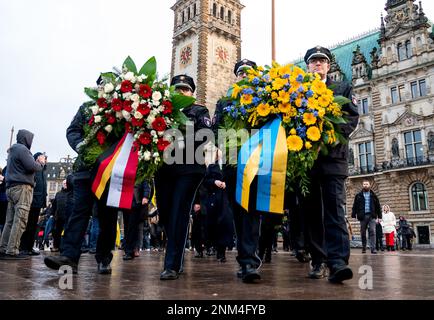 Hamburg, Deutschland. 24. Februar 2023. Polizeibeamte tragen Kränze bei einer Gedenkfeier für den Krieg in der Ukraine vor dem Rathaus. Die russische Armee war am 24.02.2022 in die Ukraine eingedrungen. Kredit: Daniel Bockwoldt/dpa/Alamy Live News Stockfoto