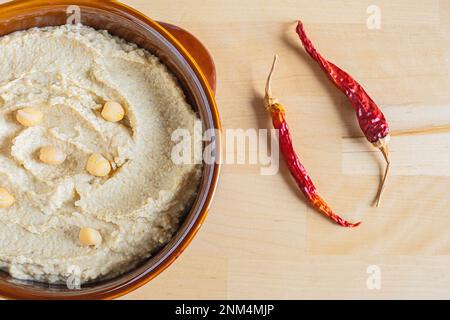 Hausgemachte Hummus-Schüssel, dekoriert mit gekochten Kichererbsen, heißem roten Pfeffer auf hellem Hintergrund. Draufsicht. Stockfoto