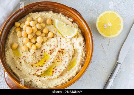 Hausgemachte Hummus-Schüssel, dekoriert mit gekochten Kichererbsen, Olivenöl, Zitrone auf hellem Hintergrund. Draufsicht. Stockfoto