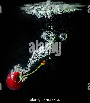 Reife Kirschen fallen ins Wasser und verursachen Spritzer und Luftblasen Stockfoto