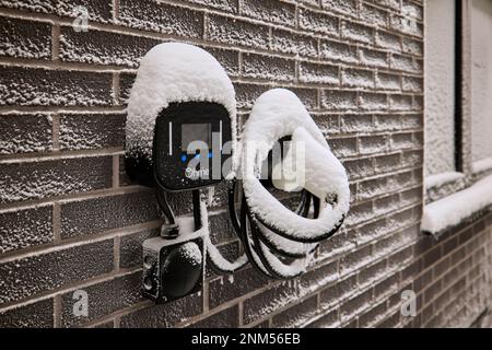 Ladestation für Elektroautos an der Außenseite eines modernen Hauses im Schnee Stockfoto