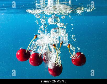 Reife Kirschen fallen ins Wasser und verursachen Spritzer und Luftblasen Stockfoto