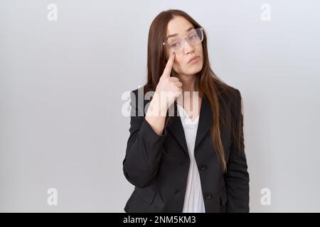 Schöne braune Frau mit Geschäftsjacke und Brille, die auf das Auge zeigt und deine Geste sieht, verdächtiger Ausdruck Stockfoto