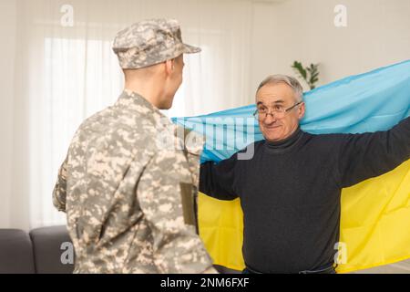 Älterer Vater und Sohn unter ukrainischer Militärflagge Stockfoto