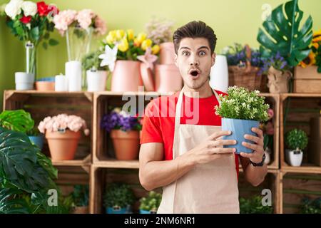 Ein junger lateinamerikanischer Mann, der im Blumenladen arbeitet und eine Pflanze in Schrecken hält. Er war begeistert von einem offenen Mund für eine Überraschung, einem ungläubigen Gesicht Stockfoto