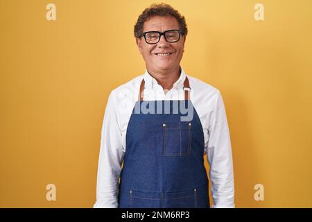 hispanischer Mann im mittleren Alter mit professioneller Kochschürze und einem fröhlichen und kühlen Lächeln im Gesicht. Glücklicher Mensch. Stockfoto