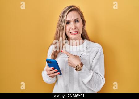 Junge blonde Frau, die eine Nachricht auf dem Smartphone tippt und mit dem Zeigefinger besorgt und nervös ist, besorgt und überraschend ausdrückt Stockfoto