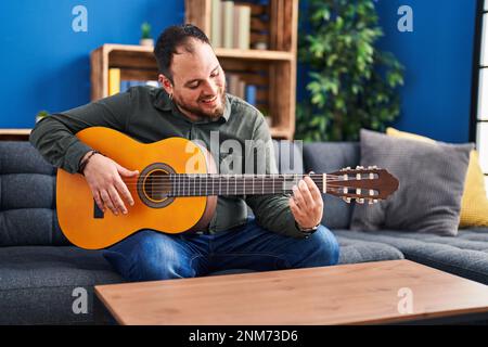 Junger hispanischer Mann spielt klassische Gitarre und sitzt zu Hause auf dem Bett Stockfoto